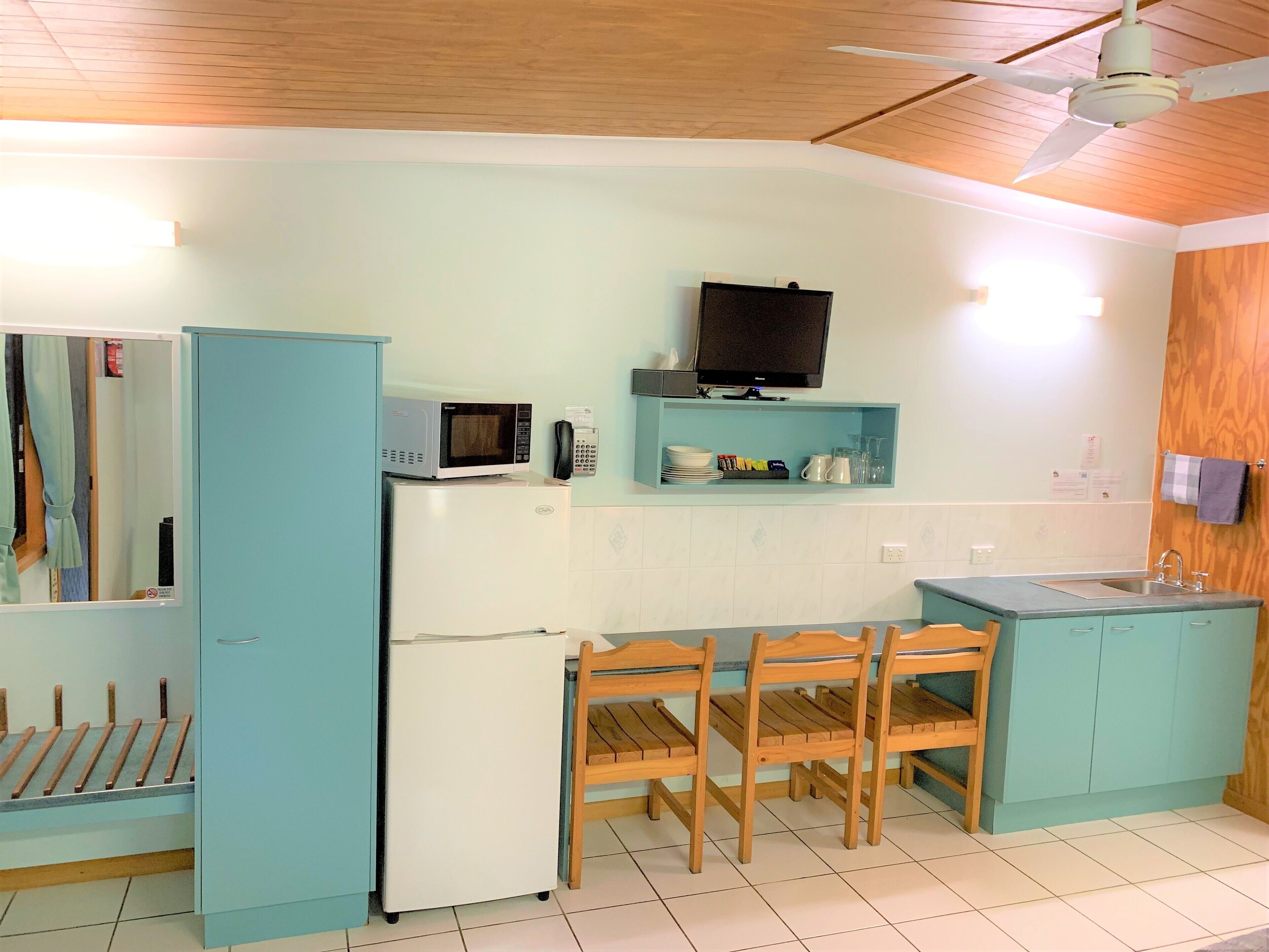 A compact kitchen with a microwave, refrigerator, wooden chairs, a small table, and a wooden cabinet.