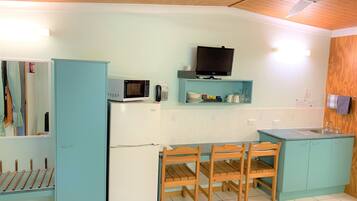 A compact kitchen with a microwave, refrigerator, wooden chairs, a small table, and a wooden cabinet.