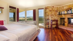 A bedroom with a large bed, a fireplace, and a view of the landscape. - Cape Otway Cottages (Hordern Vale)