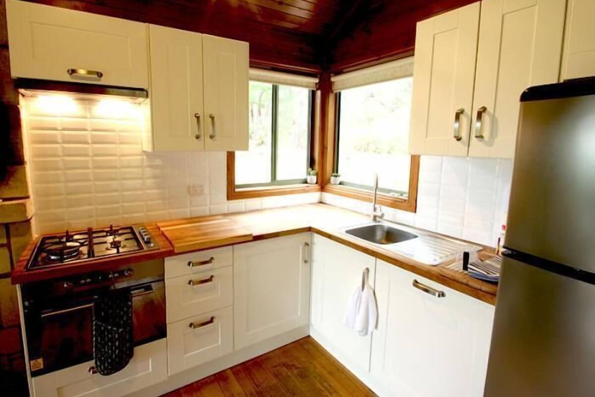 A compact kitchen with white cabinets, a wooden countertop, a stainless steel refrigerator, and a window providing natural light.