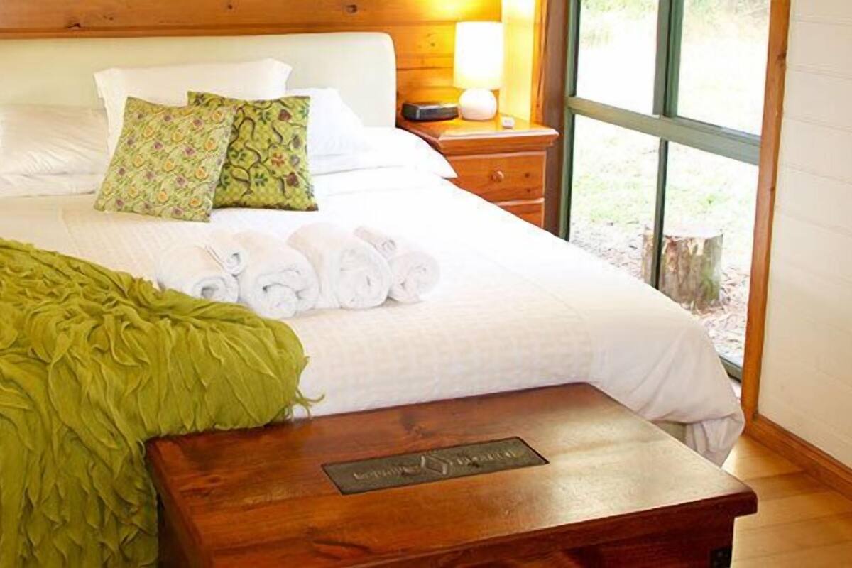 A neatly made bed with pillows and a green throw blanket, wooden headboard, bedside tables with lamps, and a large window.