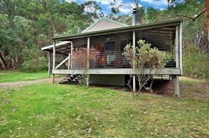 A wooden cabin with a porch, surrounded by trees and grass. - Cape Otway Cottages (Hordern Vale)