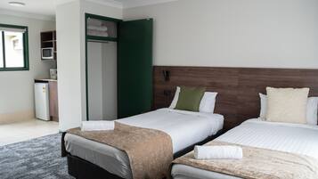 Habitación de hotel con dos camas, un escritorio, un armario y una kitchenette pequeña.