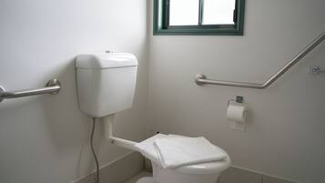 A white toilet with a towel on top, a handrail, and a window above it.