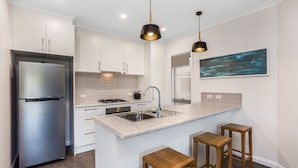 A modern kitchen with white cabinets, a stainless steel refrigerator, a sink, and wooden stools. - National Hotel Complex and Bendigo Central Apartments (Bendigo)