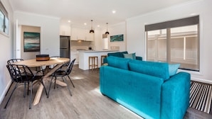 A modern living room with a teal sofa, a wooden dining table with chairs, and a kitchen in the background. - National Hotel Complex and Bendigo Central Apartments (Bendigo)
