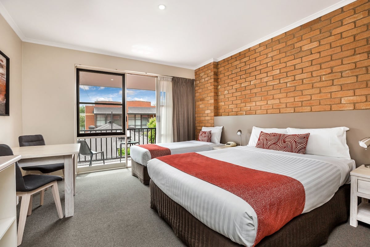 Quarto de hotel com duas camas, uma escrivaninha e varanda com vista para edifícios.