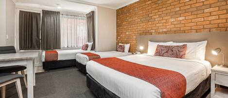 Habitación de hotel con dos camas, un escritorio y una pared de ladrillo.