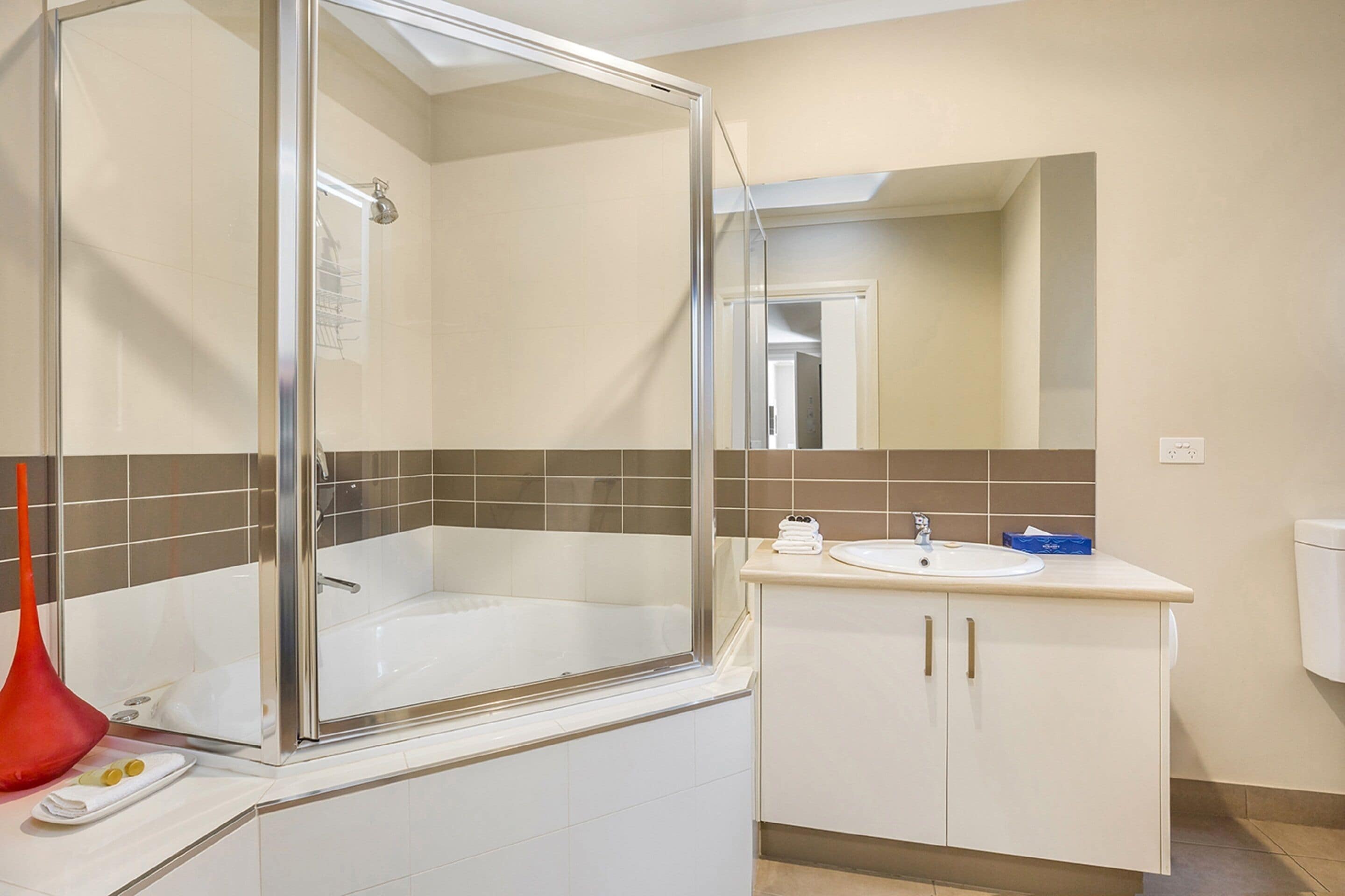 A modern bathroom with a glass-enclosed bathtub, a white sink, and a mirror above the sink.