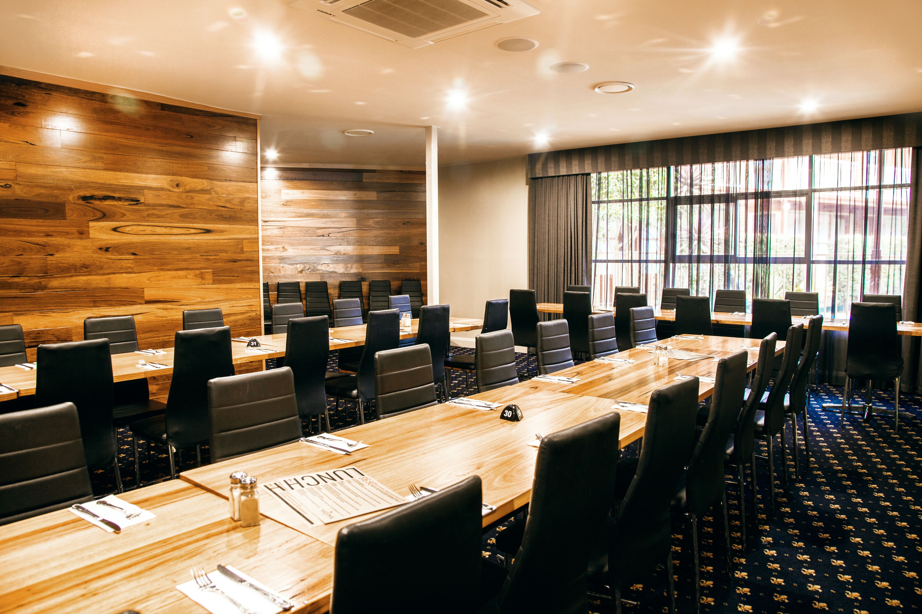 A conference room with multiple tables and chairs, wooden panel walls, and large windows with curtains.
