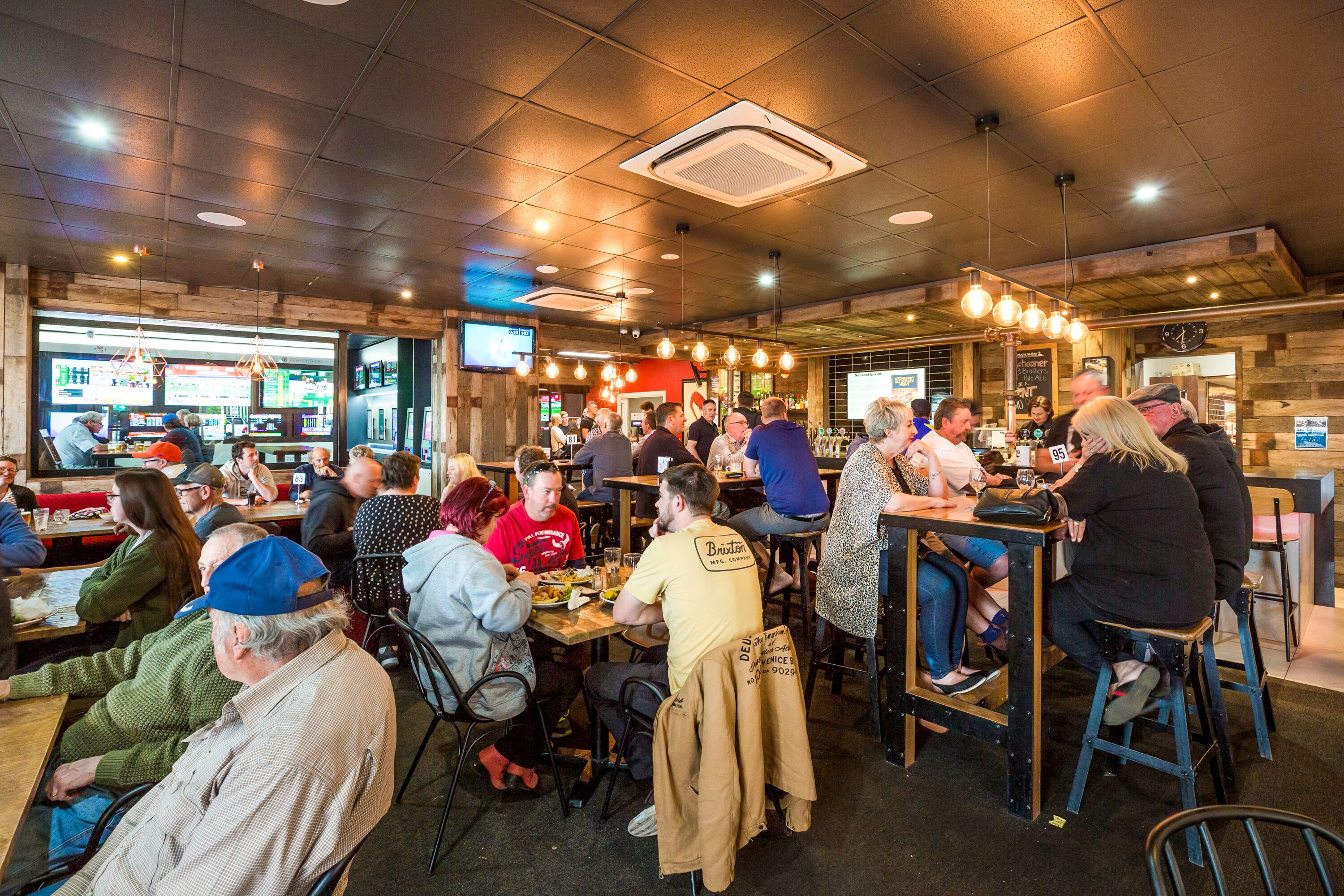 A busy restaurant with wooden interiors and multiple tables and chairs.