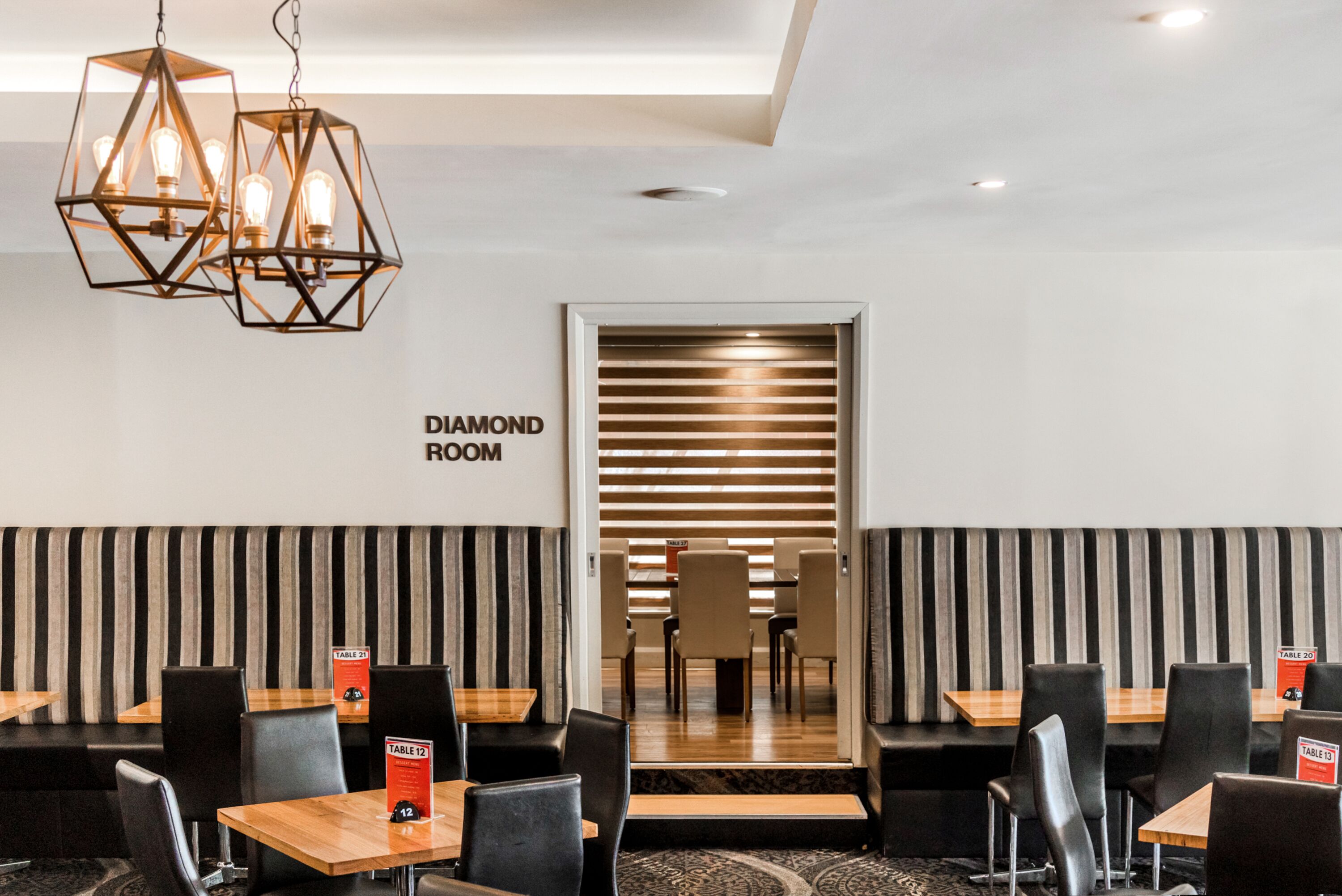 A modern dining area with hexagonal pendant lights, black and white striped walls, and a sign indicating the 'Diamond Room'.