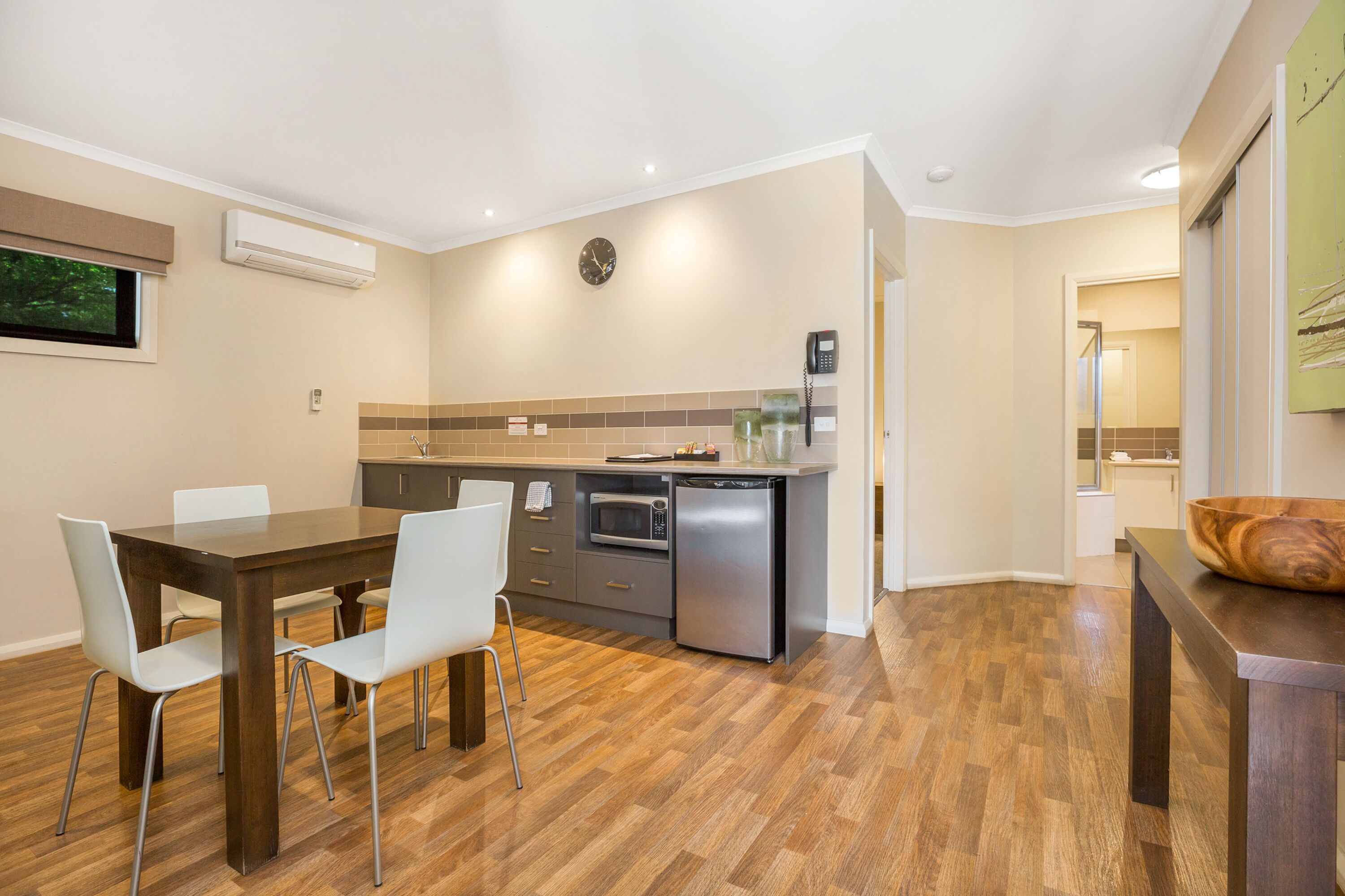 A modern kitchen with a dining area, featuring a wooden table, white chairs, a built-in oven, and a microwave.