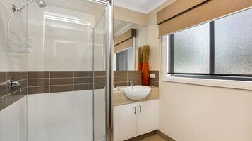 Ein modernes Badezimmer mit Duschkabine aus Glas, einem weißen Waschbecken und einem Fenster mit Blick.