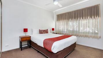 Un dormitorio con una cama, dos mesitas de noche, un ventilador de techo y una ventana con cortinas.