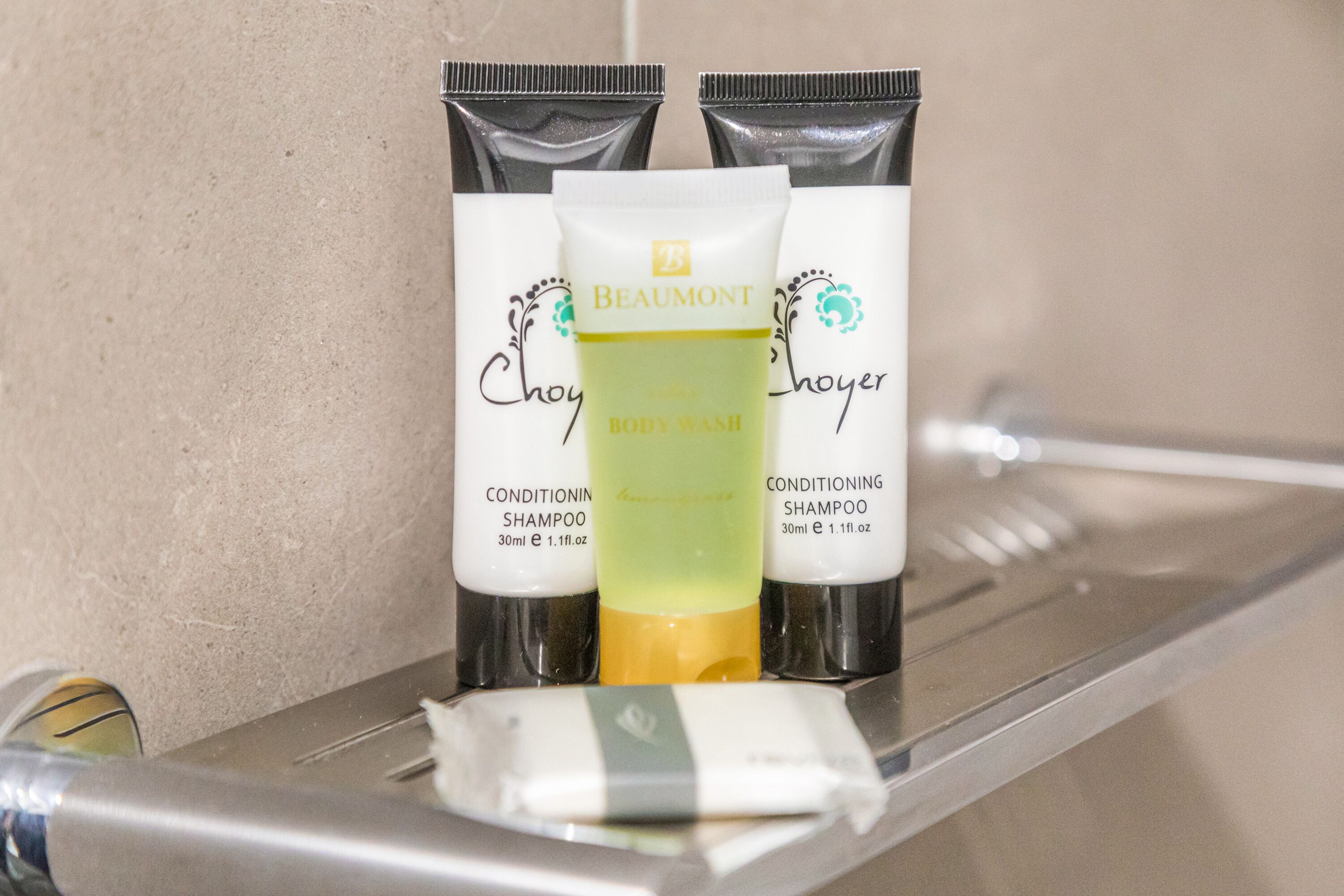 A bathroom shelf with three bottles of Beaumont body wash and two bottles of conditioning shampoo.