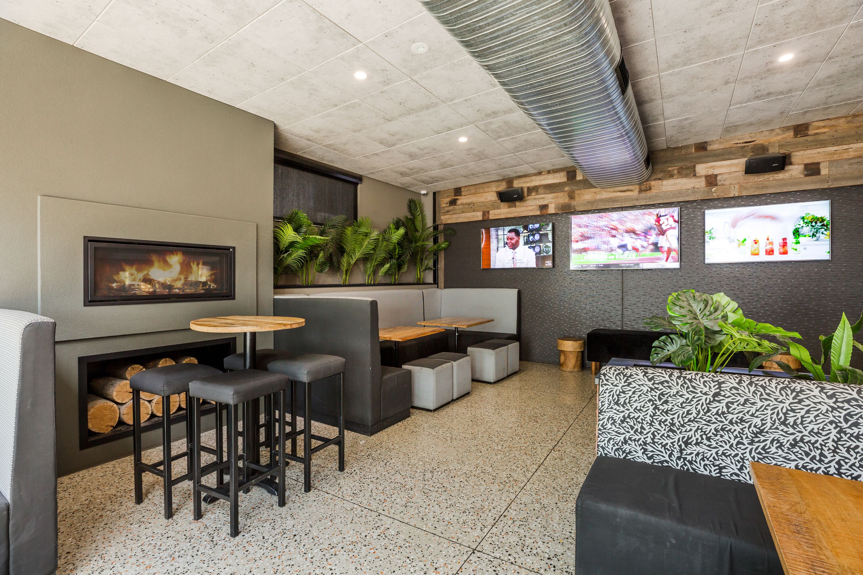 Un área de bar moderna con asientos, chimenea y televisores en la pared.