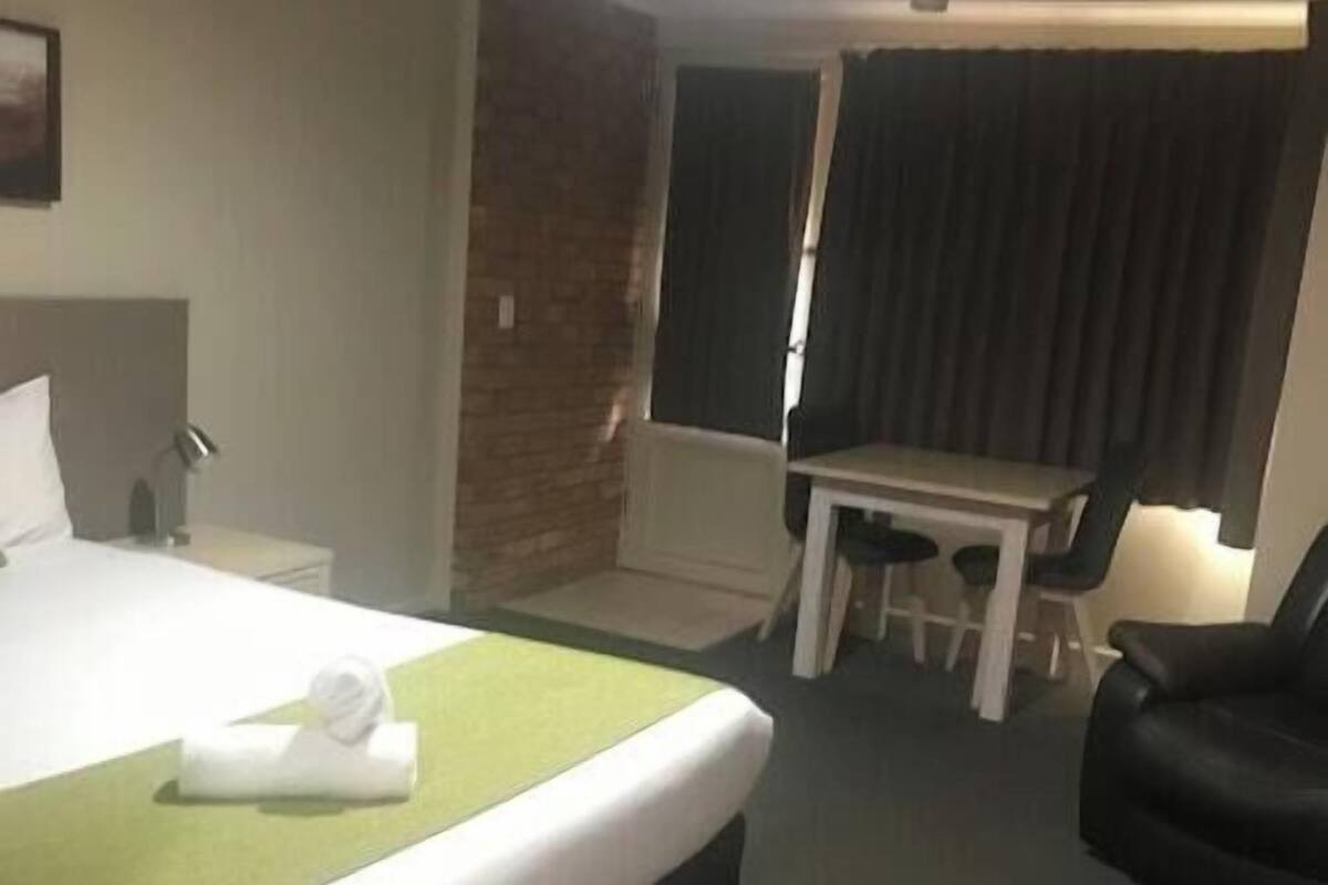Quarto de hotel com uma cama, uma escrivaninha, uma cadeira e uma poltrona de couro preto.