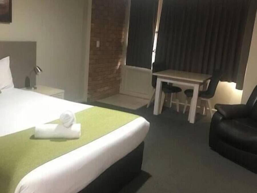 A hotel room with a bed, a desk, a chair, and a black leather chair.