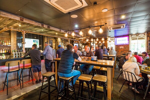 Zona de bar con taburetes, barra y una pantalla de televisión mostrando un nombre.