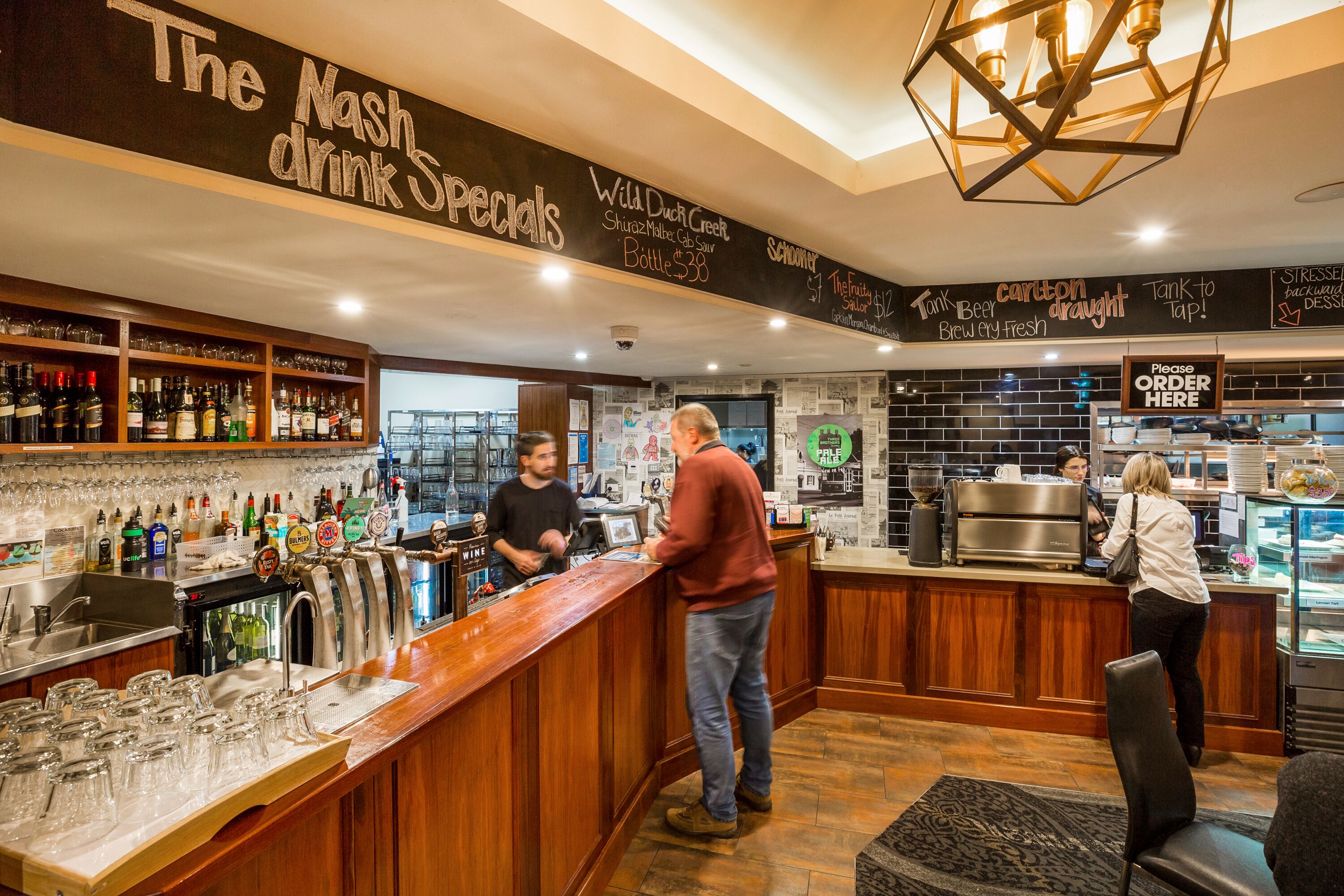 A bar area with a wooden counter, shelves with bottles, and a chalkboard menu.