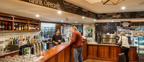 A bar area with a wooden counter, shelves with bottles, and a chalkboard menu.