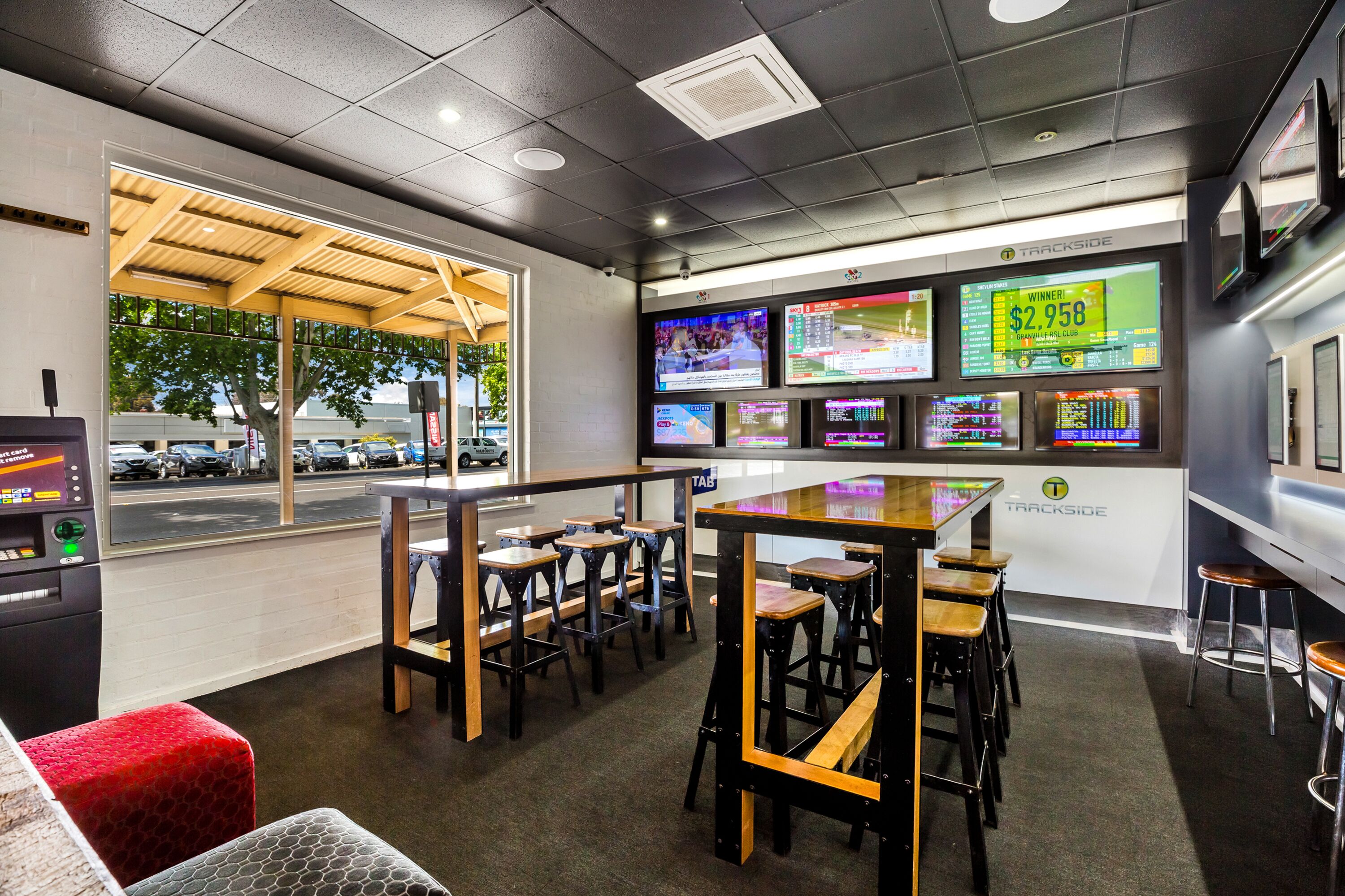 A betting shop interior with multiple screens displaying sports results, a counter, and several stools and tables.