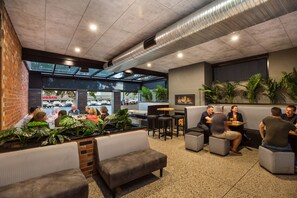 Un área de estar interior moderna con paredes de ladrillo, ventanas amplias y plantas en macetas.