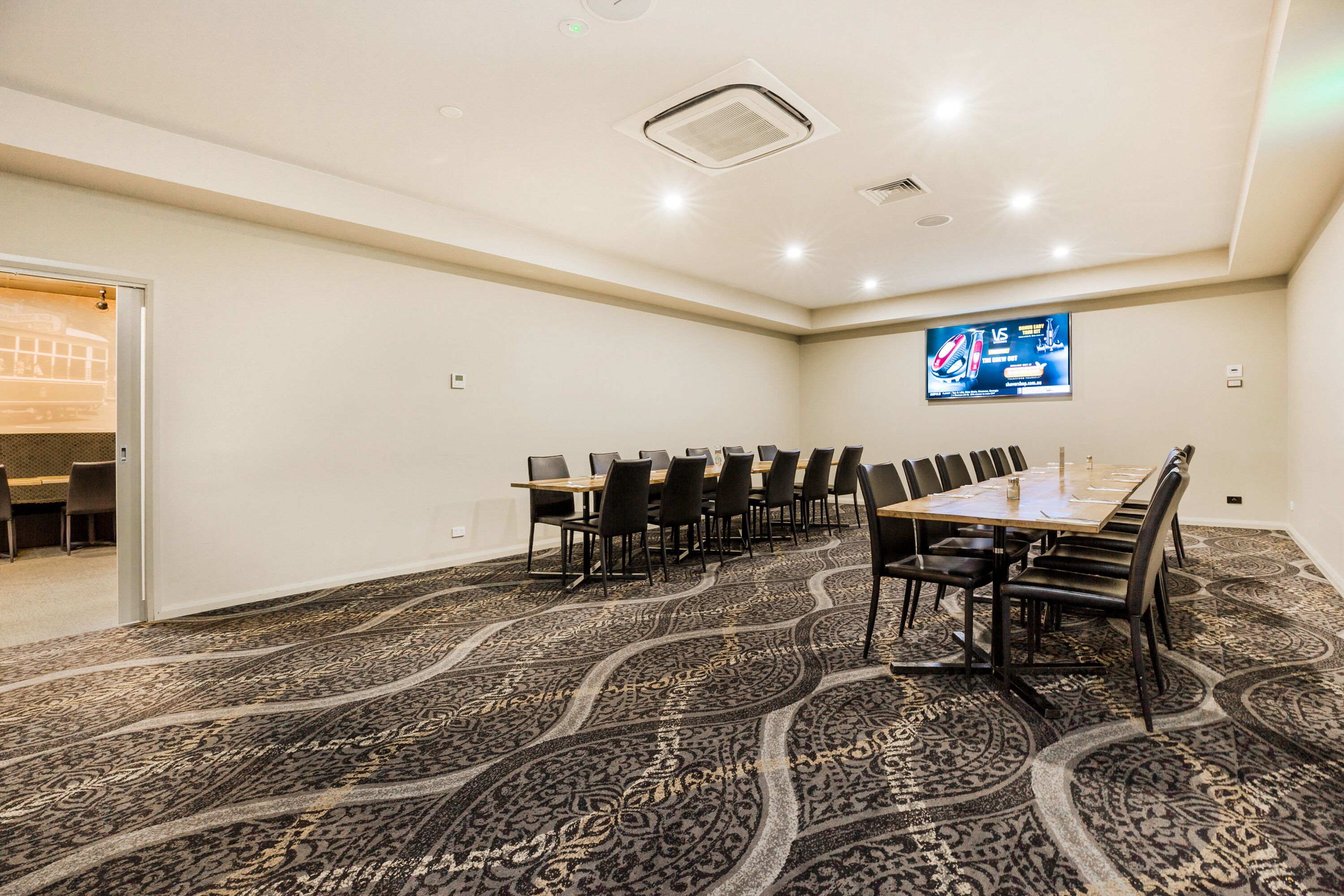 Un salón de conferencias con una gran mesa, sillas, piso alfombrado y un televisor montado en la pared.