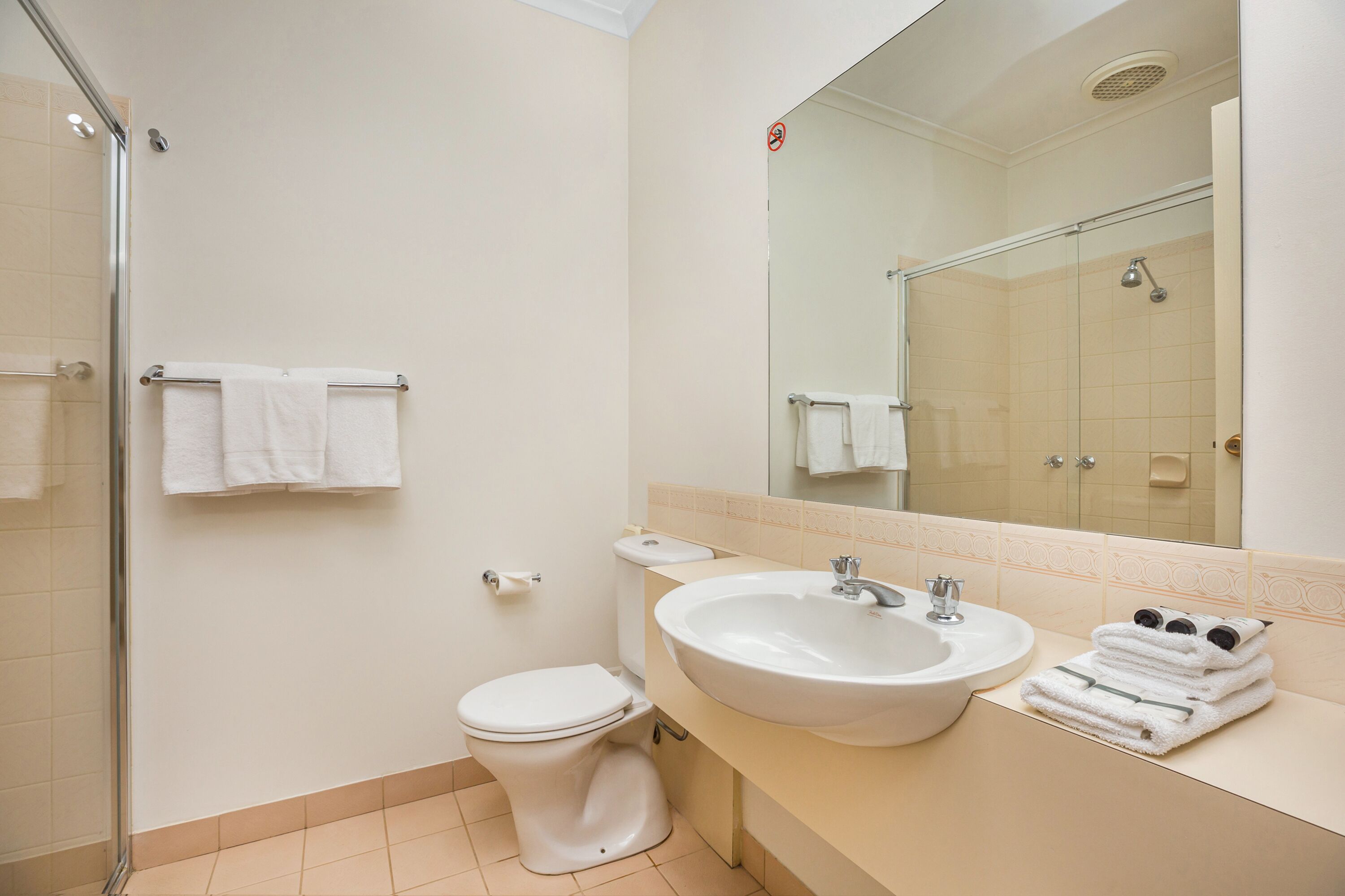 A modern bathroom with a glass shower enclosure, a white toilet, a sink with a mirror above, and neatly stacked towels.