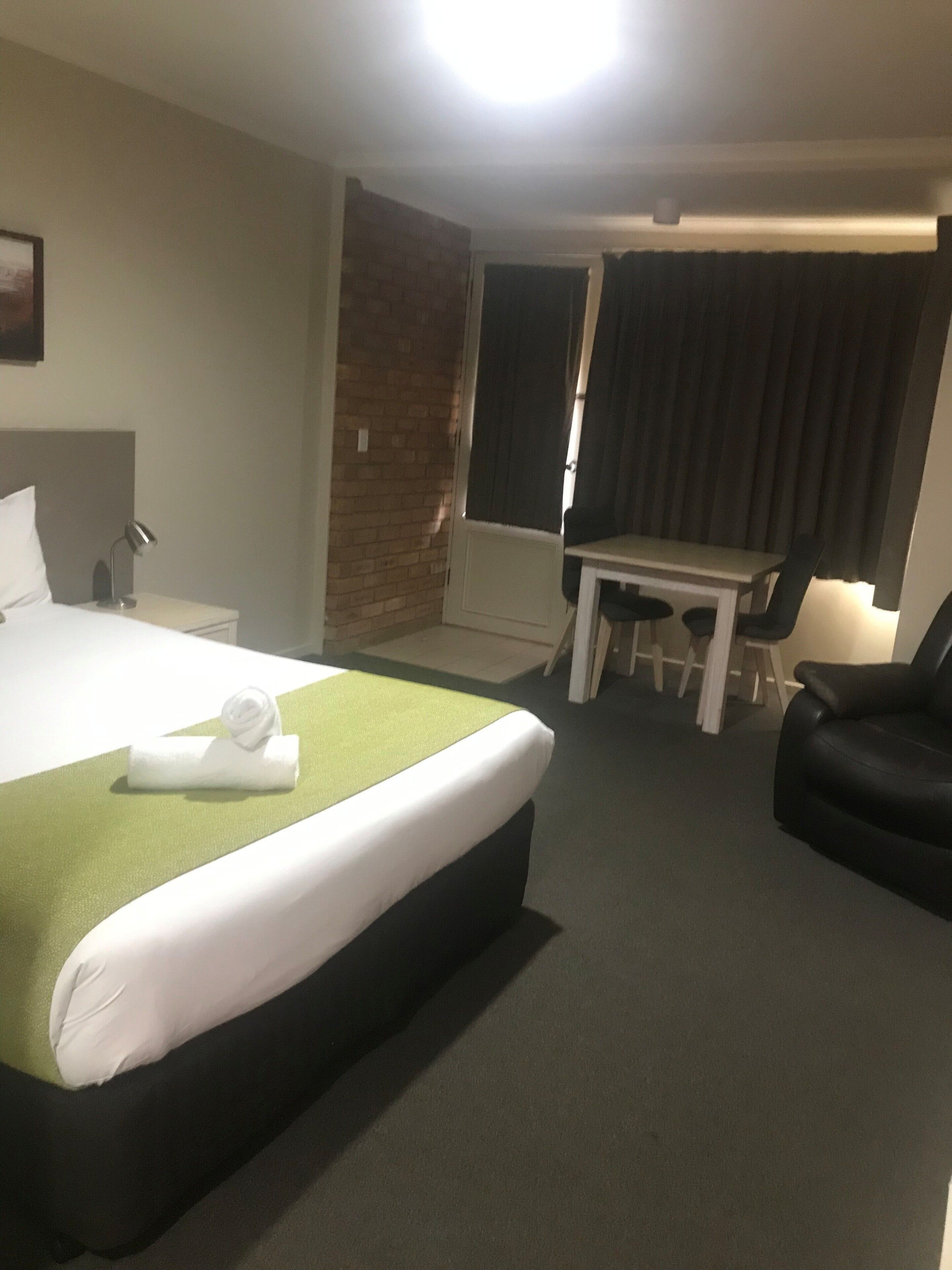 A hotel room with a bed, a desk, a chair, and a black armchair.