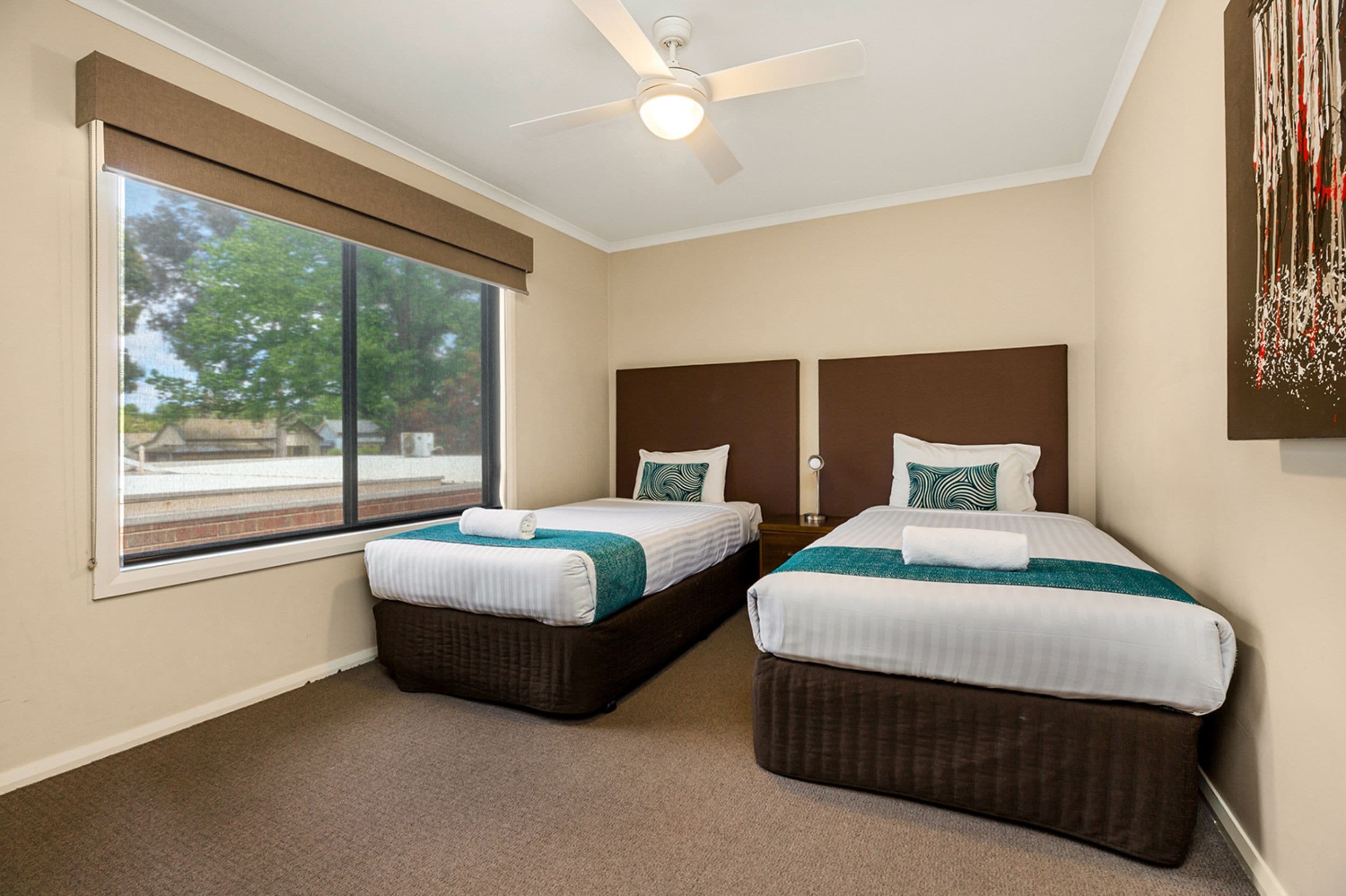Habitación de hotel con dos camas, ventilador de techo, ventana grande y vistas al exterior.
