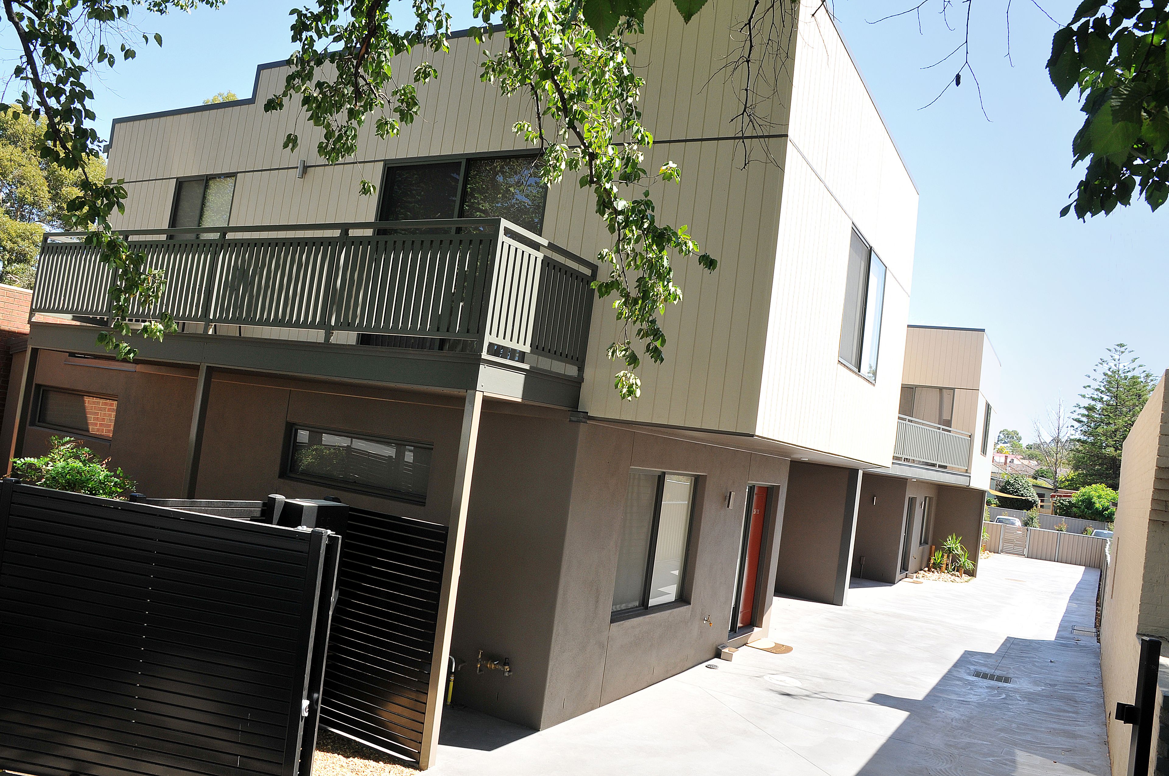 A modern two-story residential building with a balcony, a garage, and a small garden area.
