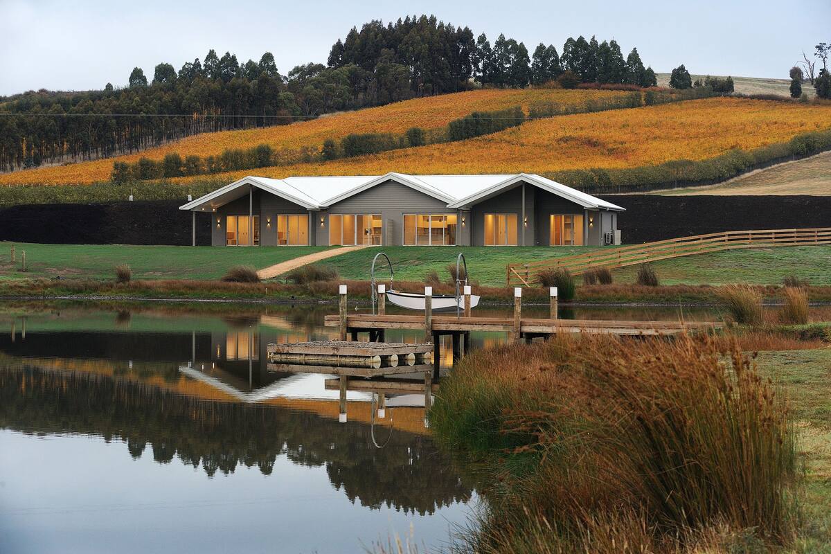A modern house with a large deck and a boat dock, surrounded by a lake and autumn foliage.