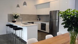 A modern kitchen with a central island, stainless steel appliances, and a dining area with a wooden table and white chairs. - Relbia Lodge (Relbia)