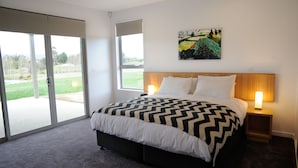 A bedroom with a large bed, two bedside tables with lamps, a sliding glass door leading to a balcony, and a painting on the wall. - Relbia Lodge (Relbia)