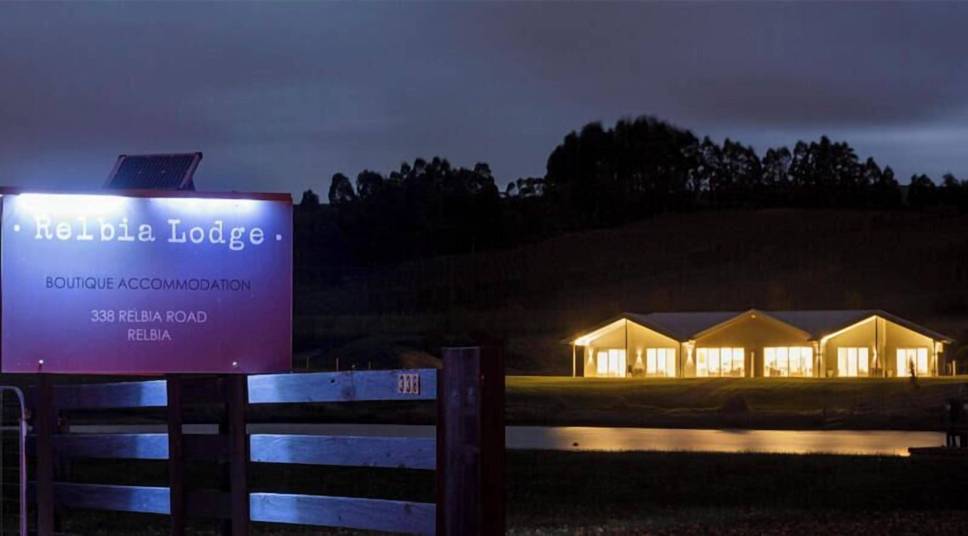 A sign for Relbia Lodge, a boutique accommodation, with a well-lit building in the background.