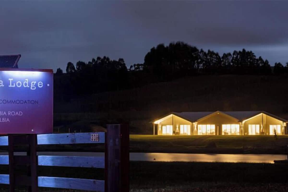 A sign for Relbia Lodge, a boutique accommodation, with a well-lit building in the background.