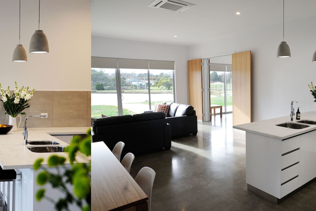A modern kitchen with a dining area, large windows, and a black sofa.