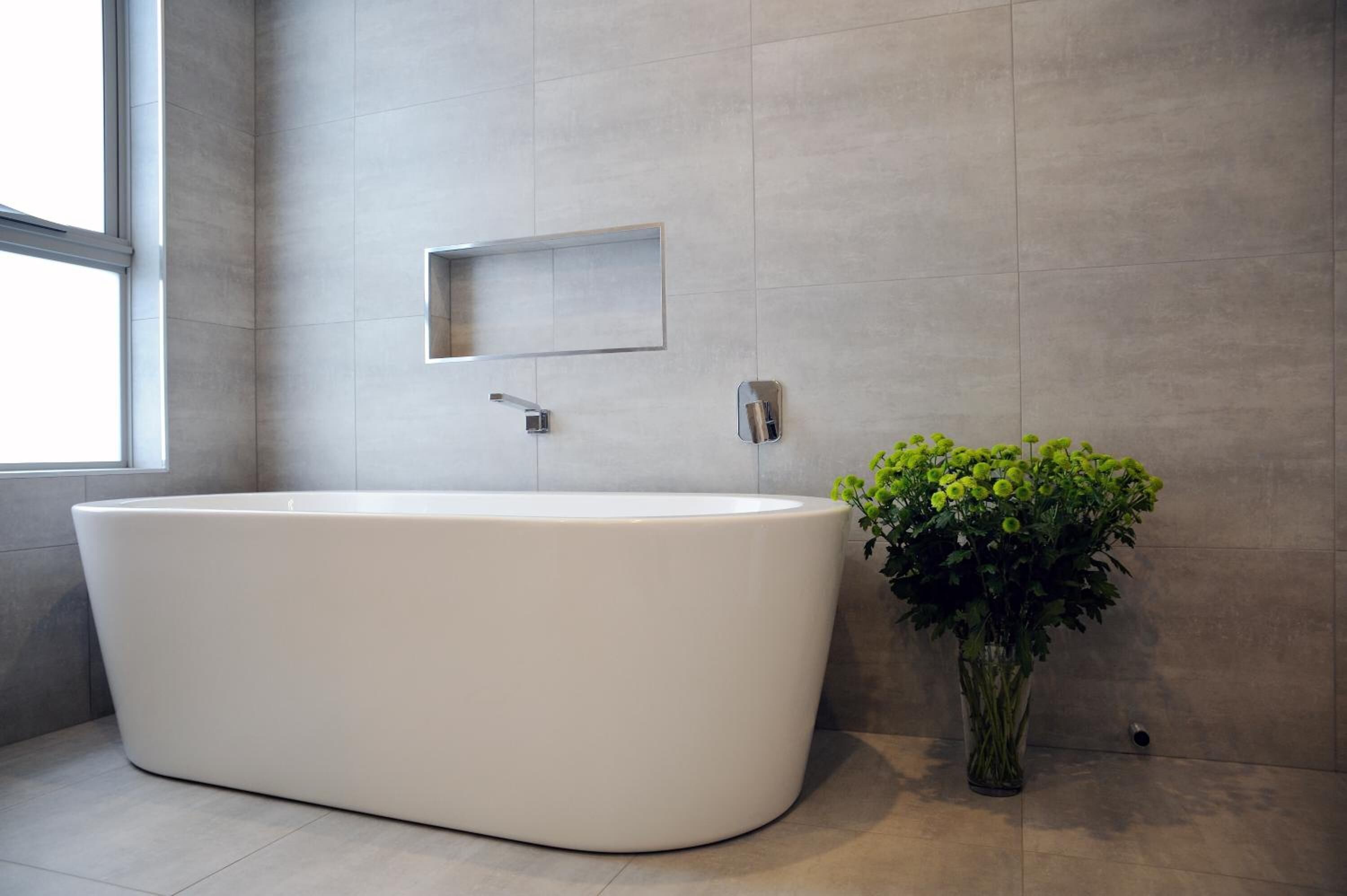 Ein modernes Badezimmer mit freistehender Badewanne, einem kleinen Spiegel und einer Topfpflanze.