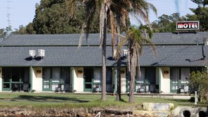 A motel with a tiled roof, outdoor seating, and a pond with swans. - Hibiscus Lakeside Motel (Budgewoi)