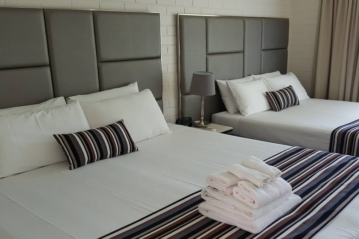 Quarto de hotel com duas camas, cada uma com colcha e almofadas listradas. Há uma pilha de toalhas dobradas na cama em primeiro plano.