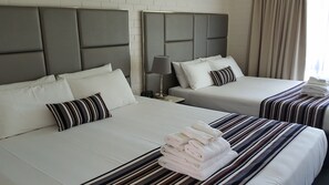 Ett hotellrum med två sängar, var och en med ett randigt överkast och kuddar. På sängen i förgrunden ligger en hög med hopvikta handdukar.