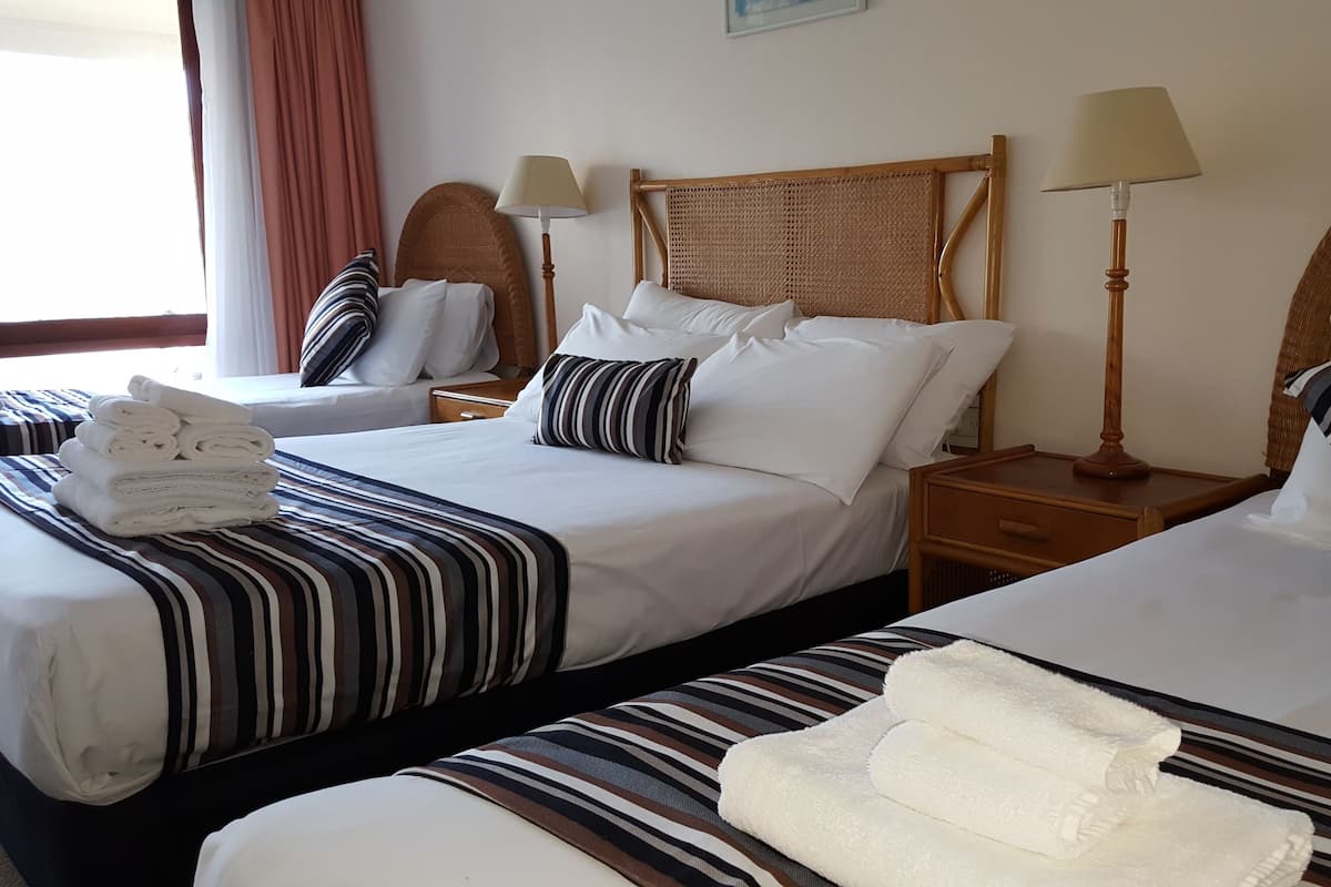 Quarto de hotel com duas camas, cada uma com roupa de cama listrada e almofadas, cabeceira de madeira, abajures e cama bem arrumada com toalhas dobradas.
