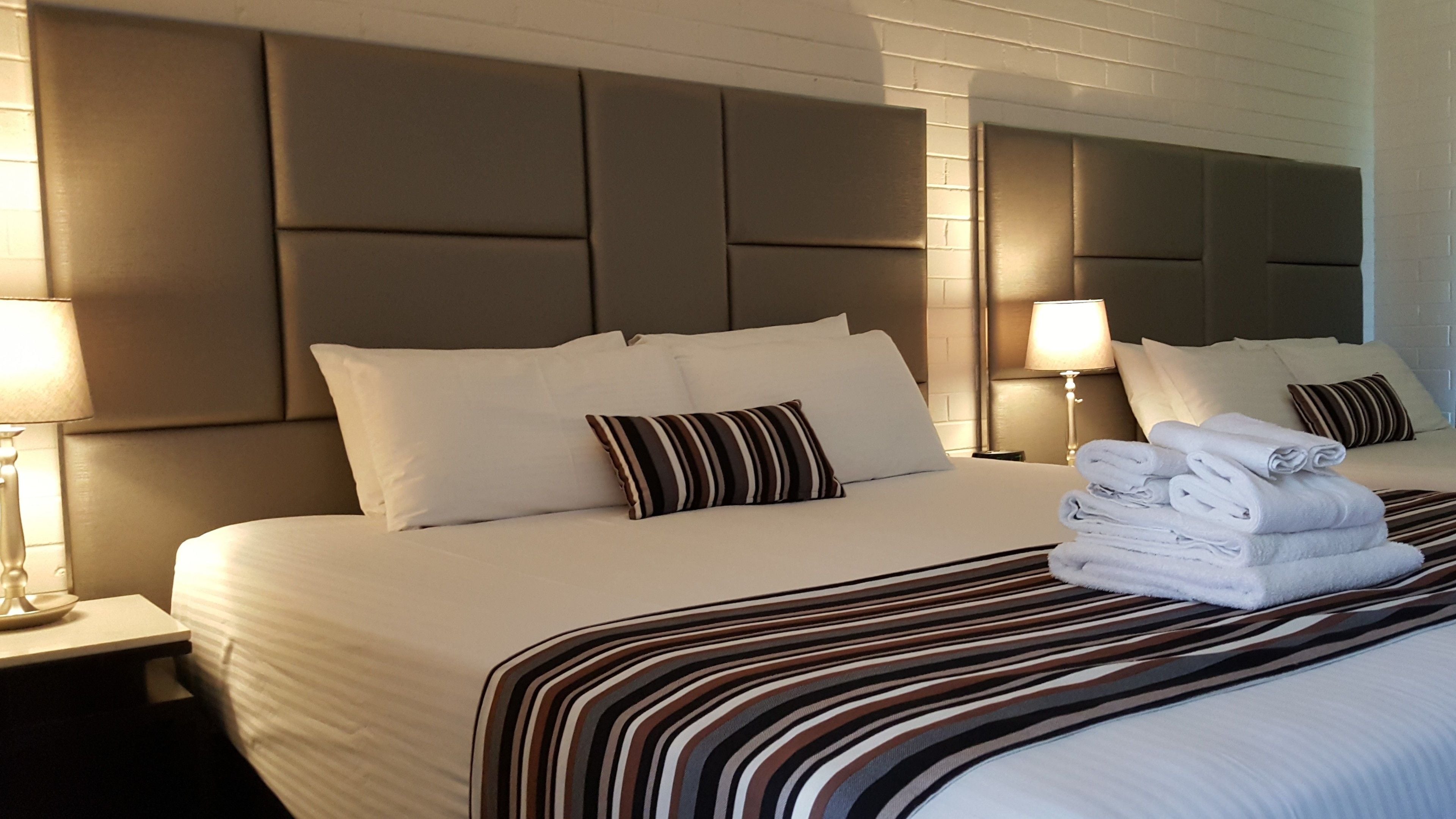 A hotel room with a large bed, a headboard, two bedside lamps, and a stack of folded towels.