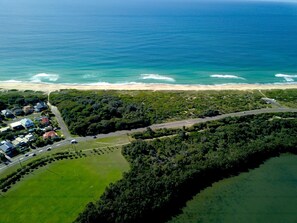 Vue aérienne d’une zone côtière comprenant une plage, une route et un quartier résidentiel avec des maisons.