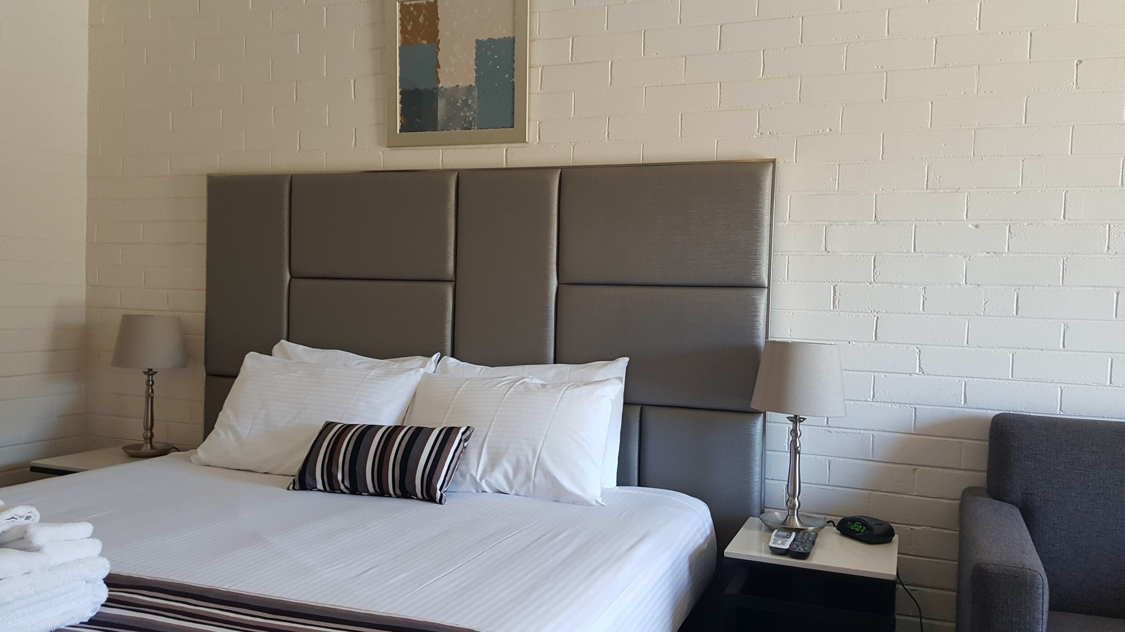 A hotel room with a large bed, two bedside tables, a chair, and a white brick wall.