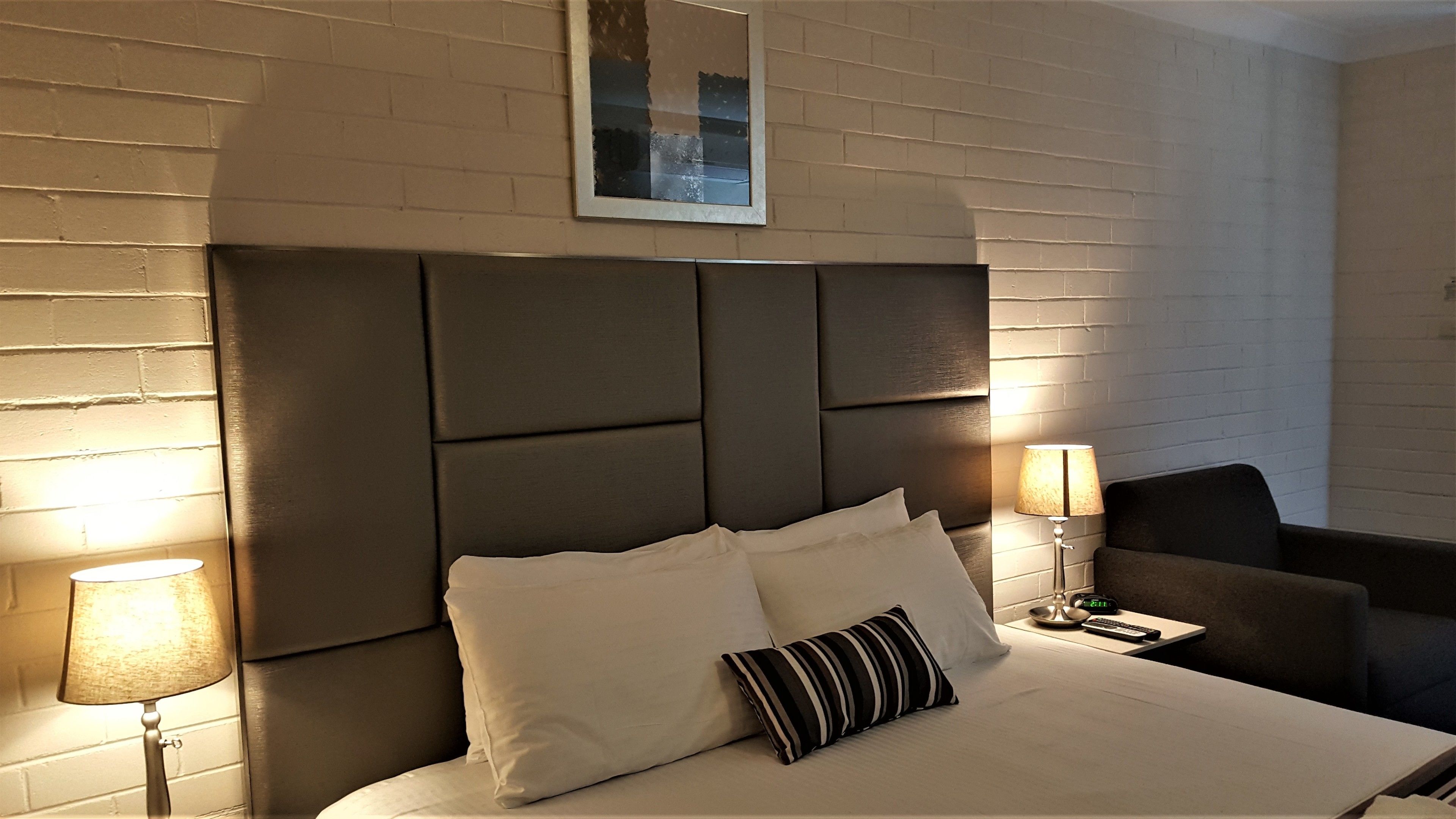 A hotel room with a large bed, two bedside lamps, a clock, and a chair.