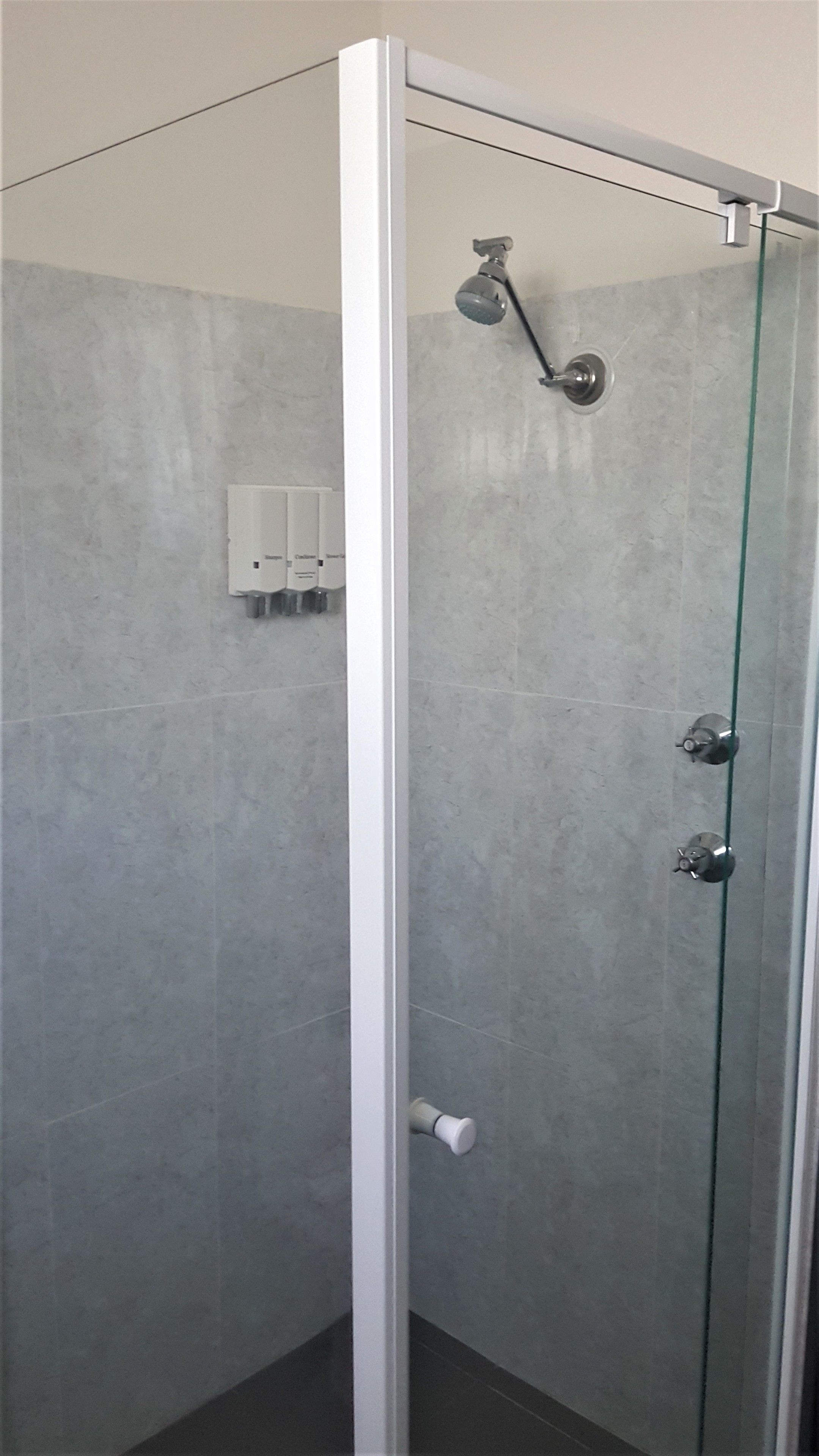 Um chuveiro com paredes de vidro, um chuveiro manual e um painel de controle fixado na parede.
