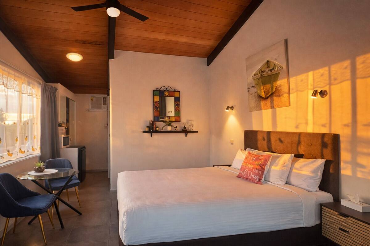 A bedroom with a bed, a desk, chairs, a mirror, and wall-mounted lights.